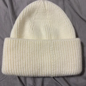 Vit ribbstickad mössa från Lager 157 - Säljer en stilren vit ribbstickad mössa från Lager 157. Mössan har en bred uppvikt kant och är tillverkad i mjukt stickat material som håller dig varm under kyliga dagar. Perfekt accessoar för att lyfta din vinterstil. (Köpte för trodde att den skulle komma till användning, men användes aldrig) priset kan diskuteras 