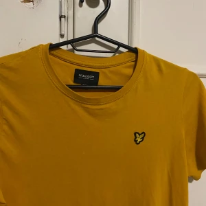 Gul t-shirt från Lyle & Scott - Snygg gul t-shirt från Lyle & Scott med klassisk rund hals och korta ärmar. På bröstet sitter den ikoniska broderade fågel-loggan i svart och gult. T-shirten är gjord i mjuk bomull och har en clean, enkel look som funkar till jeans eller shorts. ALDIDG använt o e för åldern 10-11 år 