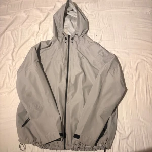 Ljusgrå vindjacka från Wrangler ATG XL - Säljer en ljusgrå vindjacka från Wrangler ATG i storlek XL. Jackan har huva, hel dragkedja framtill, justerbar nederkant med snörning och praktiska fickor med dragkedja. Perfekt för blåsiga dagar och outdoor-äventyr.