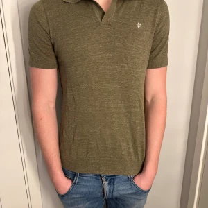 Morris pike  - Snygg olivgrön pikétröja med kort ärm och klassisk krage. Tröjan har en diskret broderad logga på bröstet och är tillverkad i ett mjukt, stickat material som känns skönt mot huden. Perfekt för en avslappnad och stilren look.