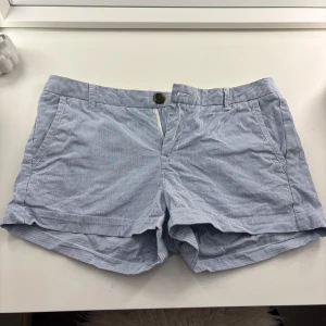 Randiga blå shorts från L.O.G.G. - Snygga blå och vita randiga shorts från L.O.G.G. med klassisk midja och knappstängning. De har fickor på sidorna och är gjorda i mjuk bomull, perfekta för varma dagar. Passar dig som gillar en chill och fräsch stil.