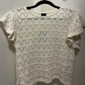 Vit stickad blus med volangärm - Säljer en vit stickad blus med korta volangärmar och ett snyggt hålmönster över hela tröjan.