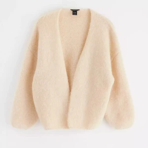 Beige fluffig kofta  - Supermjuk och oversized beige kofta. Den har en öppen front utan knappar, breda ärmar och är stickad i ett fluffigt material som känns lyxigt och mysigt. Perfekt att slänga på sig när det är kyligt ute.