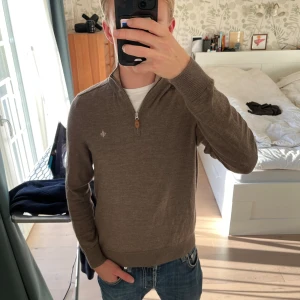 Brun half zip tröja från Morris - Säljer en brun stickad tröja från Morris med half zip och liten broderad logga på bröstet. Tröjan har hög krage, ribbade muddar och är tillverkad i mjuk ull. Perfekt för lager-på-lager och snygg till jeans. Enda defekten är lappen i tröjan som är borta, annars mycket bra skick!