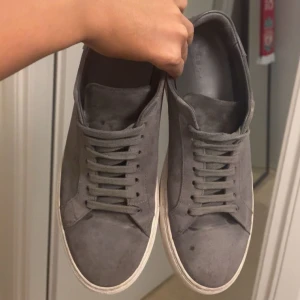  Axel Arigato, clean 90 - Snygga grå sneakers från Axel Arigato med låg profil och platt vit sula. Skorna har rund tå, snörning och är tillverkade i mocka med detaljer i skinn på hälen. Perfekt för dig som gillar stilrena sneakers.  Skorna tillkommer med box och dustbag, samt påsen om man vill göra meetup. Skorna har tecken på användning, mockan har fått sämre kvalité, dessutom har den ena skon fått en skvätt färg vilket sänker värdet . Nypris: 2700kr. Pris kan diskuteras! 