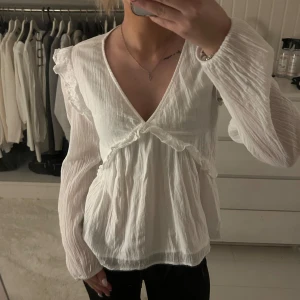 Vit blus med volang och v-ringning - Supersöt vit blus från Gina Tricot med v-ringning, långa ärmar och volangdetaljer vid axlar och byst. Blusen är gjord i ett tunt, lätt och skrynkligt bomullstyg som ger en luftig känsla. Perfekt att styla, super fin blus och super söt . Använda fåtal gånger! Storlek 170/xs! Inga fläckar eller hål! Pris: 200kr 