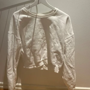 Vit croppad sweatshirt - Enkel och stilren vit croppad sweatshirt med rund halsringning och långa ärmar. Tröjan har en avslappnad passform och är tillverkad i mjuk bomull, perfekt för en chill och clean look.