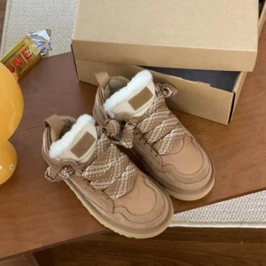 Beige boots med fuskpäls och snörning - Säljer ett par beige boots med platt sula och rund tå. Skorna har snörning med mönstrade band och är fodrade med vit fuskpäls för extra värme. Perfekta för kalla dagar och har en chunky look som är riktigt trendig.