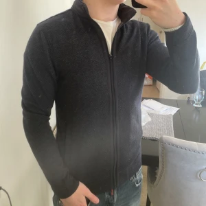 Massimo dutti kofta/cardigan - Väldigt fin Massimo dutti kofta i storlek S. Väldigt fint skick. Runt kragen finns en dragkedja och går att öppna och ta ut en luva i vindsskydds material. I fickorna är det även material som är någon typ av vindskyddande. Blå, svart och grå är koftan.