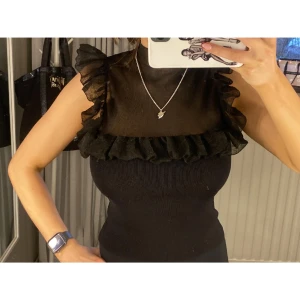 Svart volangblus med mesh - Säljer en svart blus med mesh upptill och volangdetaljer över axlar och bröst. Knappt använd. Storlek S 