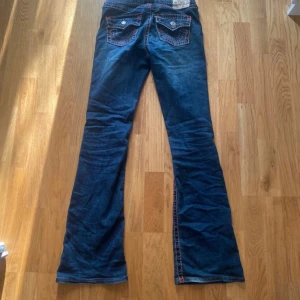 True Religion Becca Bootcut Jeans - Snygga blå jeans från True Religion, modell Becca Mid Rise Bootcut. Jeansen har vinröda kontrastsömmar. Bootcut passform och midwaist men är som low waist! Perfekt för dig som gillar detaljer och lite annorlunda jeans än de vanliga true religion. Använda typ 7 gånger och nypris 2399kr. Tror inte jeansen säljs längre då jag inte hittat de någonstans!