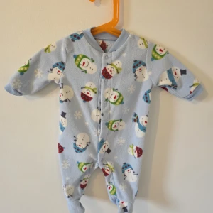 Blå fleecepyjamas med snögubbar Carter's - Supermjuk blå fleecepyjamas från Carter's med gulligt snögubbemönster i olika färger. Pyjamasen har långa ärmar, tryckknappar framtill och ribbade muddar vid hals och ärmslut. Perfekt för mysiga vinterkvällar! När jag försökte köra noppbortagare, blev halsen skadat tyvärr. Se bild. 