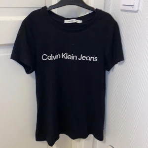 Svart Calvin Klein Jeans t-shirt XS - Svart t-shirt från Calvin Klein Jeans i storlek XS. Klassisk modell med rund halsringning och vit logga tryckt framtill. Tillverkad i mjuk bomull för en skön känsla. Perfekt till jeans eller shorts för en clean och enkel look. KÖPTE FÖR 300 SÄLJER FÖR 150