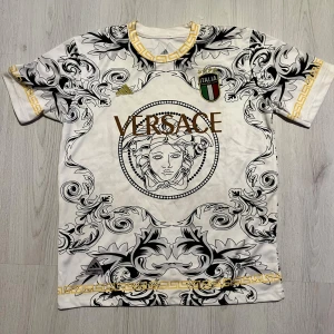 Italien Adidas fotbollströja - Snygg vit fotbollströja från Adidas  och stora svarta barockmönster. Guldiga detaljer runt hals och ärmslut, samt Italiens klubbmärke på bröstet. Tillverkad i lätt och ventilerande polyester (Climalite).