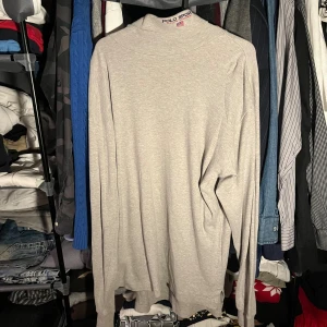 Grå polotröja från Polo Sport - Snygg grå polotröja från Polo Sport Ralph Lauren i mjuk bomull. Tröjan har lång ärm och klassisk polokrage, perfekt för dig som gillar enkel och clean stil. Passar dig som vill ha en basic men ändå stilren look.