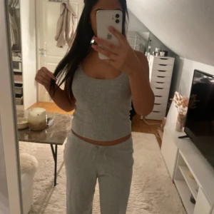 Grått set i ribbat material - Säljer en ljusgrå ribbad linnetopp med smala axelband och spetsdetaljer längs kanterna. Toppen är croppad och har en mjuk, stretchig känsla som gör den superbekväm. Perfekt att matcha med mjukisbyxor för en chill look. Med kommer ett par matchande byxor.