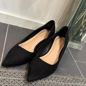 Svarta pumps med spetsig tå från Anna Field - Säljer ett par klassiska svarta pumps från Anna Field i mocka-look. Skorna har spetsig tå, låg klack och en stilren design som passar till många outfits. Insidan är ljusbeige och sulan är svart. Perfekta för dig som gillar en elegant och tidlös stil.