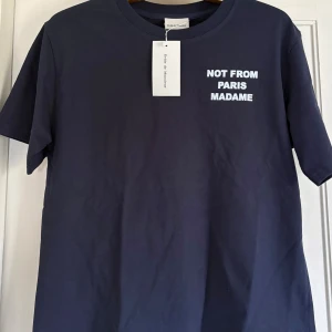 Mörkblå t-shirt Drôle de Monsieur, NOT FROM PARIS MADAME - Mörkblå t-shirt från Drôle de Monsieur med vit text 'NOT FROM PARIS MADAME' tryckt på både bröstet och ryggen. Tillverkad i mjuk bomull, perfekt för en chill och stilren look.