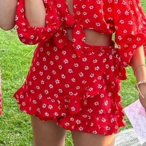 Röd blommig skort Zara S - Supersöt röd omlottkjol med inbyggda shorts från Zara med vita blommor och volangkant. Kjolen har dragkedja bak, knyt i sidan och är kort i modellen. Obs säljer bara nedre delen, ej toppen, men den går säkerligen att köpa separat av nån annan☺️