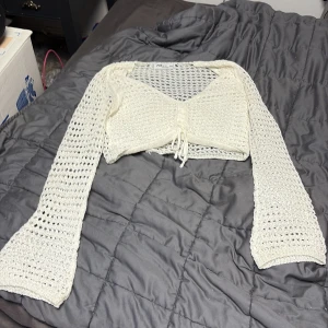 Vit stickad bolerotopp från new yorker  - Säljer en vit stickad bolerotopp från new yorker i storlek XXS. Toppen har långärmade, genombrutna ärmar och croppad passform med knyt framtill. Materialet är stickat och luftigt