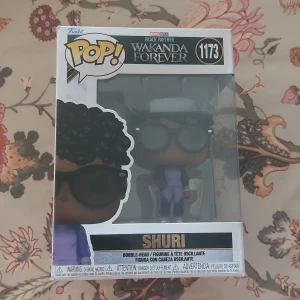 Funko Pop! Shuri 1173 Black Panther Wakanda Forever - Funko Pop! figur av Shuri från Black Panther: Wakanda Forever, nr 1173. Figuren är i nyskick och levereras i originalförpackning, perfekt för samlare och Marvel-fans. Inga synliga defekter eller slitage på boxen.