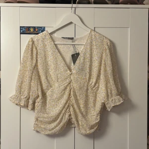 Blommig blus med v-ringning från ONLY - Säljer en söt blommig blus från ONLY i ljusgul och vit med små blommor. Blusen har v-ringning, rynkade detaljer framtill, trekvartsärmar med volangkant och smock baktill. Perfekt för vår och sommar, superfin till jeans eller kjol! Storleken är XL men skulle säga att den sitter jättefint som en lite oversized blus på folk med storlek xs-m också. Jag brukar ha xs eller S i tröjor och tycker den här sitter fint.