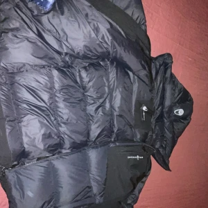 Sail racing (sail Antarctica) jacka XL - Svart pufferjacka från Sail Racing i storlek XL. Tillverkad i polyester och dun, perfekt för kalla dagar. Snygga detaljer med logga på armen och bröstet. Riktigt varm och stilren vinterjacka. Har aldrig ägt en varmare jacka än denna, har använt 3/4 veckor under vintern. Finns i Växjö/lessebo