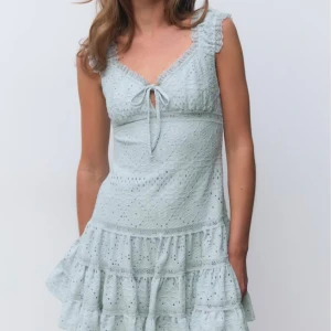 Ljusblå spetsklänning med volanger - Superfin ljusblå klänning med spetsdetaljer och volanger. Klänningen har v-ringning med söt knytning framtill och är ärmlös med volangkant vid axlarna. 