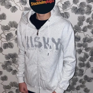 Ljusgrå hoodie från Risky  - Säljer en ljusgrå hoodie från Risky i storlek XS. Tröjan har dragkedja framtill, huva med vita snören och ett stort tryck med texten 'RISKY' i grått över bröstet. Perfekt för en chill och avslappnad stil. Aldrig använd. Skriv vid minsta fundering ✅fraktar inom 24h 💨📦