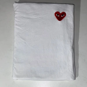 Vit Comme des Garçons Play t-shirt - Säljer två vita t-shirt från Comme des Garçons Play i storlek M och L. T-shirten har ett ikoniskt rött hjärta med ögon broderat på bröstet. Klassisk rund hals och korta ärmar. Tillverkad i mjuk bomull för skön komfort och clean look. Kom med frågor eller pris förslag, vid snabb affär 399kr!!