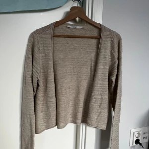 Beige stickad kofta från ONLY - Säljer en beige stickad kofta från ONLY i storlek L. Koftan är öppen framtill, har lång ärm och är tillverkad i ett tunt, mjukt material med diskret ribbad struktur. Perfekt att slänga över en topp för en chill look.