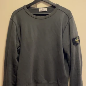 Grå Stone Island sweatshirt S - Säljer en olivgrön sweatshirt från Stone Island i storlek S. Tröjan har rund halsringning, långa ärmar och den klassiska Stone Island-loggan på vänster ärm. Tillverkad i mjuk bomull för skön komfort och clean look.