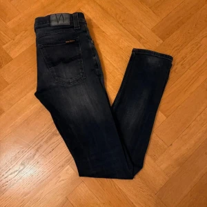 Mörkblå jeans från Nudie Jeans - Snygga mörkblå jeans från Nudie Jeans med klassisk femficksdesign och diskret tvättade detaljer. Modellen har rak passform och normal midja, med Nudie-logga på bakfickan och läderpatch i midjan. Perfekt för dig som gillar stilrena och tidlösa jeans.