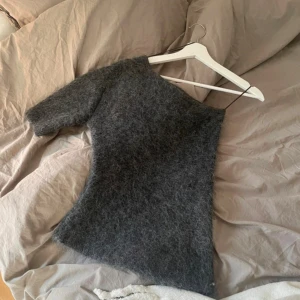 Mörkgrå stickad oneshoulder topp Zara - Säljer en fluffig mörkgrå stickad topp från Zara i oneshoulder-modell. Toppen har en unik asymmetrisk form med en ärm och är tillverkad i mjukt stickat material som ger en cool och trendig vibe. Perfekt för dig som gillar att sticka ut med din stil. Godkänner alla prisförslag!💞