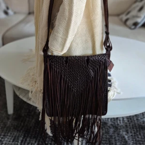 Läderväska med fransar * hippie / bohem * nyskick - Perfekta julklappen! Unik mörkbrun läderväska/axelremsväska med flätat mönster och långa fransar.  * Justerbar axelrem.  * Ett fack med dragkedja på insidan samt ett utan.  * Nyskick. Använd två ggr (för många väskor)  * Höjd 28 cm, bredd 26 cm. Exkl fransarna.   Djur och rökfritt hem. Se bilder och förstora då de ingår i beskrivningen.  Se gärna mina övriga annonser. 