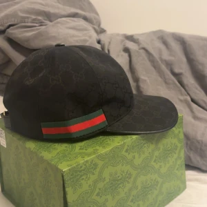 Svart Gucci keps med logga och ränder - Snygg svart keps från Gucci med diskret GG-monogram över hela kepsen, nytt skick. Alla tillbehör finns 