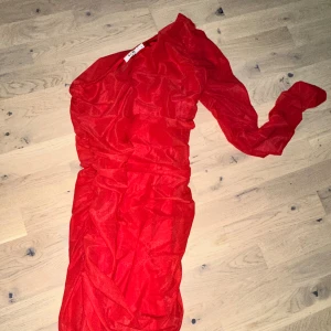 Röd långklänning från NA-KD oneshoulderNA-KD röd klänning, storlek M - Säljer en snygg röd långklänning från NA-KD i storlek M. Klänningen har oneshoulder-design med lång ärm på ena sidan och är tillverkad i ett lätt, glansigt syntetmaterial. Den har draperade detaljer som ger en cool och trendig look.Röd klänning med en ärm och draperad design. Perfekt för festliga tillfällen - jul - nyår . 
