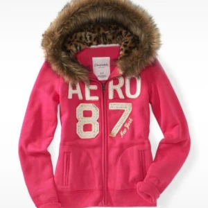 Fur zip up från Aeropostale - Snygg rosa hoodie från Aeropostale med dragkedja, stora broderade bokstäver och siffror framtill. Huva med fuskpäls och leopardmönstrat foder ger extra stilpoäng. Perfekt för kyliga dagar och 2000s vibe!👠🐆💕 Stolek L men sitter som en S!💞 postar inom 3 arbetsdagar!👛
