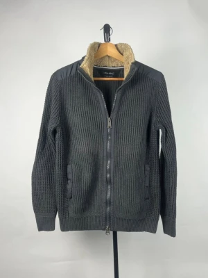 Cardigan - Mörkgrå stickad cardigan från Marc O'Polo med dragkedja framtill och mjukt teddyfoder i kragen. Snygga quiltade axelpartier och två fickor. Perfekt för kyliga dagar och riktigt skön att bära.                      !!STORLEK M FITS S/XS!!
