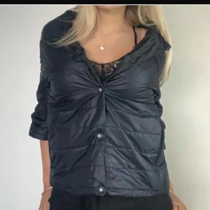 Söt jacka  - Snygg marinblå pufferjacka med glansig yta och stora knappar framtill. Jackan har en cool twistad detalj vid bröstet och en lite bredare krage. Perfekt för dig som gillar en modern och chill stil.