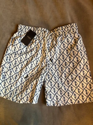 Blåvita mönstrade shorts från Fendi - Snygga shorts från Fendi i storlek XL med blått och vitt mönster. De har elastisk midja och snörning framtill. Helt nya med prislapp kvar.