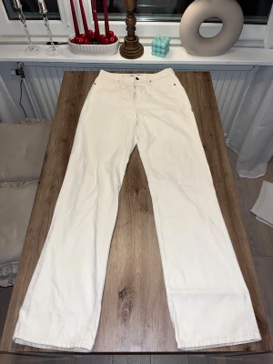 Wide jeans med hög midja - Säljer ett par beiga jeans med hög midja och wide fit. Klassisk femficksmodell med knappgylf och raka ben. Materialet är kraftig bomull som ger en clean och fräsch look. Perfekta för dig som gillar en avslappnad men trendig stil.