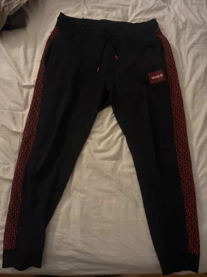 Hugo Boss svarta byxor - Svarta/Röda mjukisbyxor från Hugo i storlek XL men passar L. Stryk dom en gång så ser dom ut som nya igen. Nypris: 1300kr