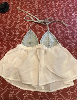 Vit och denim linnetopp  - Supersöt linnetopp från Pull&Bear med ljusblå denim-triangelkupor och vit, voluminös nederdel. Toppen har knytband i nacken och baktill för perfekt passform. Perfekt för sommardagar när du vill sticka ut med en unik och trendig look.