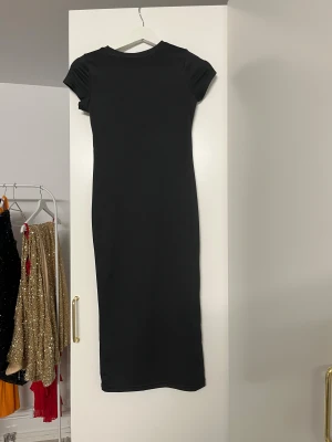 Svart långklänning med kort ärm - En stilren svart långklänning med korta ärmar och rund hals. Klänningen har en rak och slim passform som ger en snygg siluett. Perfekt för dig som gillar minimalistisk design och vill ha en enkel men elegant look.