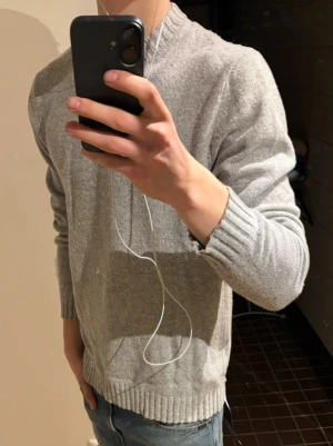 Grå stickad tröja från East West - Snygg grå stickad tröja från East West i mjuk lammull. Tröjan har ribbade muddar vid ärmslut och nederkant samt en klassisk rund hals. Perfekt för dig som gillar enkel och stilren look med lite oversized känsla.den är lite skrynklig på bilderna men de går att lösa. skriv vid funderingar eller frågor✌🏼