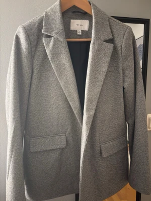 Grå rutig kavaj från Vila, strl 38 - Snygg grå kavaj från Vila i storlek 38 med diskret rutigt mönster. Klassisk krage, två fickor framtill och helfodrad insida. Perfekt för dig som gillar stilrena och tidlösa plagg med en modern touch. Jag som jag storlek S/xs vanligtvis kan ha denna