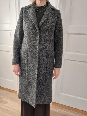 Grå kappa från KappAhl, storlek S - Säljer en snygg gråmelerad kappa från KappAhl i storlek S. Rak modell med klassisk krage, stora fickor framtill och knäppning. Materialet är 65% polyester och 35% ull, fodret är 100% polyester. 