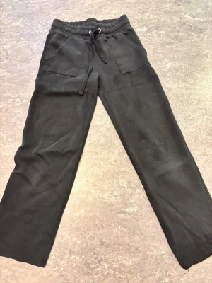 Svarta lager 157 byxor - Svarta mjukisbyxor med bred resår i midjan och snörning framtill. Byxorna har raka ben, stora fickor fram och två bakfickor. Perfekta för chill eller häng med kompisar. Materialet är mjukt och skönt, troligtvis bomull eller polyester. Dock har den fläckar och är sliten och därför kan pris diskuteras 