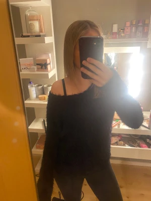 Svart fluffig offshoulder tröja - Säljer en svart fluffig tröja med offshoulder-design och långa ärmar. Tröjan har en loose passform och är supermysig, perfekt för att ge en chill och trendig vibe. Materialet är mjukt och ger en cool look som passar till jeans eller leggings.
